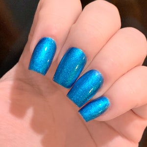 May include: Close-up of a hand with five fingernails painted in a bright blue shimmery nail polish.