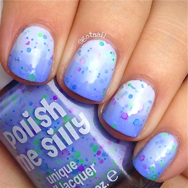 May include: Close-up of a hand with five fingernails painted with a light blue to white ombre nail polish with iridescent glitter. The bottle of nail polish is labeled "Polish Me Silly" with a heart and the words "unique lacquer" on the label.