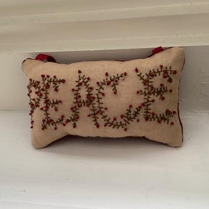 May include: A small, beige pillow with red trim and the word "PEACE" embroidered in green and red thread.