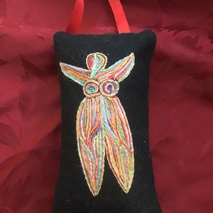 May include: A black felt pouch with a colorful embroidered figure of a person with outstretched arms. The pouch has a red ribbon attached.