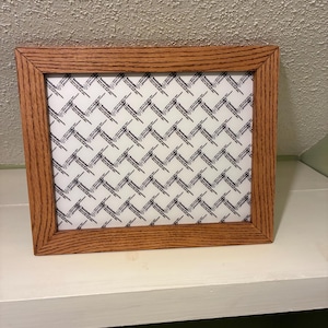 May include: A rectangular wooden picture frame with a medium brown wood grain finish. The frame contains a white insert paper featuring a repeating black graphic pattern of small arrows and the text Remindable in a grid layout.