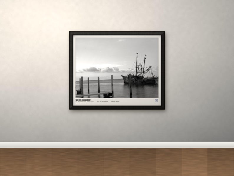 May include: A black and white framed print featuring a fishing boat docked near wooden pilings in calm water. The text "MOBILE FISHING BOAT" is printed at the bottom left of the image, along with additional small text and a square icon in the corner.
