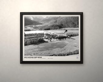 May include: A black and white framed print featuring a seaplane flying over a landscape with mountains, trees, and water. The text at the bottom reads WDE154 WATERFOWL SURVEY AIRPLANE, U.S. FISH AND WILDLIFE SERVICE, DEC. 10, 1953, ALASKA, PHOTO BY ARCHIVE.