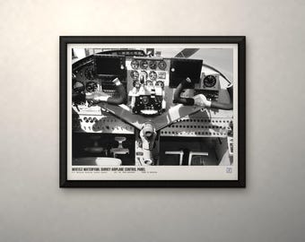 May include: A black and white framed print of an airplane cockpit control panel. The image features a central yoke, numerous circular gauges, and digital displays. Text at the bottom reads: WOE153 WATERFOWL SURVEY AIRPLANE CONTROL PANEL.