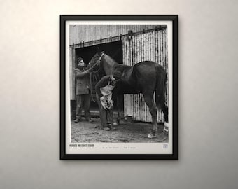May include: A black and white framed photograph titled HORSES IN COAST GUARD, depicting a person in a coat and hat holding a horse while another person in an apron works on the horse's hoof in front of a corrugated metal building.