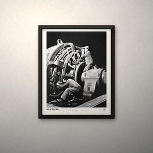 K&ouml;nnte beinhalten: Ein schwarz-wei&szlig; gerahmtes Foto, das zwei Arbeiter bei der Bedienung gro&szlig;er Industriemaschinen im Sollac-Stahlwerk zeigt. Der Druck enth&auml;lt den Text SOLLAC STEEL MILL, U.S. National Archives (public domain) sowie weiteren kleinen Text am unteren Rand.