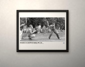 May include: A black and white framed photograph titled PHOTOGRAPH OF THE CHRISTMAS DAY BASEBALL GAME 1943. The image depicts a baseball game in progress with a batter holding a bat, a catcher crouching, and spectators in the background.