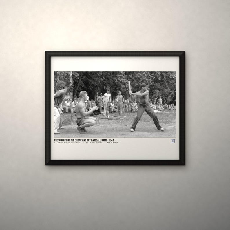 May include: A black and white framed photograph titled PHOTOGRAPH OF THE CHRISTMAS DAY BASEBALL GAME 1943. The image depicts a baseball game in progress with a batter holding a bat, a catcher crouching, and spectators in the background.
