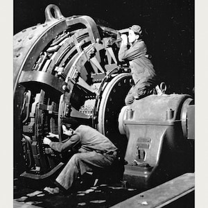 K&ouml;nnte beinhalten: Ein schwarz-wei&szlig;es Archivfoto des Sollac-Stahlwerks, das zwei Personen bei der Arbeit an einer gro&szlig;en Industriemaschine zeigt. Das Bild enth&auml;lt am unteren Rand den Text SOLLAC STEEL MILL, U.S. National Archives und ACC. NO. 0024-19982395.