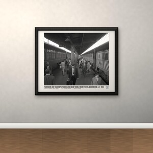 Peut inclure: Une photographie encadr&eacute;e en noir et blanc d'un quai de gare avec des passagers et des employ&eacute;s marchant pr&egrave;s des trains. Le texte en bas indique : PASSENGERS AND TRAIN EMPLOYEES WALKING NEAR TRAINS, UNION STATION, WASHINGTON, D.C. 1963.
