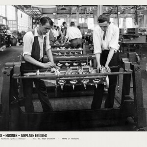 May include: A black and white archival photograph showing two individuals in a factory setting working on an airplane engine mounted on a metal frame. The text at the bottom reads: AIRPLANES - ENGINES - AIRPLANE ENGINES U.S. National Archives.