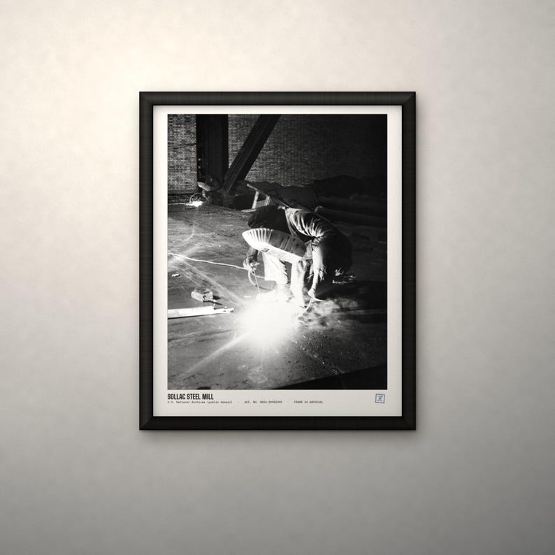 May include: A black and white framed print titled SOLLAC STEEL MILL, featuring a worker welding in a dark industrial space. The bright light from the welding torch illuminates the floor, while the text at the bottom provides details about the scene.