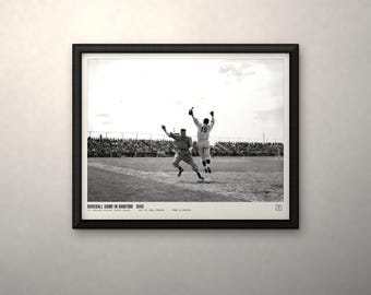 May include: A black and white framed photograph of a 1945 baseball game in Hanford. The image shows two players in uniform on a dirt field, one jumping to catch a ball. Text at the bottom reads BASEBALL GAME IN HANFORD 1945.