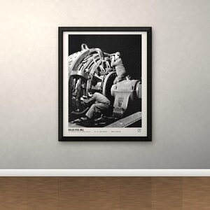 K&ouml;nnte beinhalten: Ein schwarz-wei&szlig;er gerahmter Druck mit einer historischen Fotografie von Arbeitern, die schwere Maschinen im Dollac Steel Mill bedienen. Das Bild zeigt Industrieanlagen und Arbeiter in einer dunklen Umgebung, mit Text am unteren Rand des Drucks.
