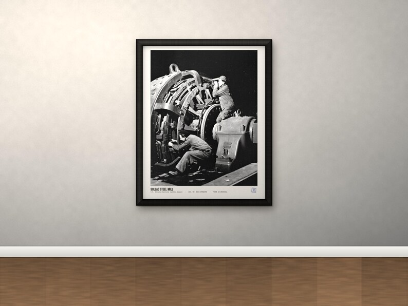 K&ouml;nnte beinhalten: Ein schwarz-wei&szlig;er gerahmter Druck mit einer historischen Fotografie von Arbeitern, die schwere Maschinen im Dollac Steel Mill bedienen. Das Bild zeigt Industrieanlagen und Arbeiter in einer dunklen Umgebung, mit Text am unteren Rand des Drucks.