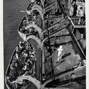 May include: A black and white photograph showing a boat drill on a ship deck with multiple lifeboats suspended by davits. Sailors are positioned in the boats and on the deck. Text at the bottom reads: BOAT DRILL BEFORE SAILING U.S. National Archives (public domain) . ACC. NO. 0024-05583518 . FRAME 24 ARCHIVAL.
