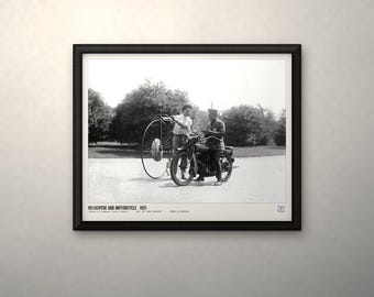 May include: A black and white framed print titled VELOCIPEDE AND MOTORCYCLE 1921. The image depicts a person standing next to a large-wheeled velocipede and another person seated on a motorcycle, with text at the bottom of the print.