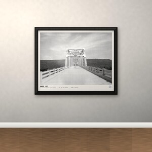 May include: A black and white framed wall art print featuring a perspective view of a truss bridge. The text at the bottom reads BRIDGE 1937, followed by smaller text including the location and date. The print is enclosed in a black frame.