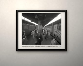 May include: A black and white framed photograph of Union Station in Washington, D.C. in 1963, showing passengers and employees walking between trains. The text at the bottom reads: PASSENGERS AND TRAIN EMPLOYEES WALKING NEAR TRAINS, UNION STATION, WASHINGTON, D.C. 1963.