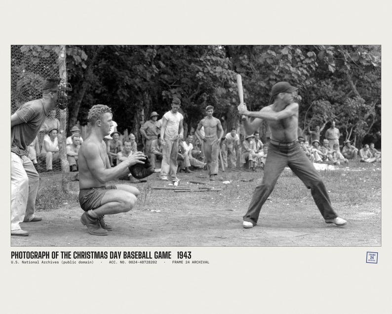 May include: A black and white historical photograph titled PHOTOGRAPH OF THE CHRISTMAS DAY BASEBALL GAME 1943. It depicts a baseball game in progress with a batter holding a wooden bat, a catcher in a crouched position, and spectators.