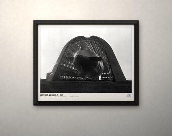 May include: A black and white framed print featuring a large airship inside a hangar. The text ARC-1933-A91-0261-15 1933 is printed at the bottom. The image shows the rear view of the airship structure within the arched hangar frame.