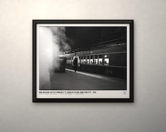May include: A black and white framed photograph titled MAN WALKING ON PLATFORM NEXT TO TRAIN IN STATION, NEW YORK CITY 1959. The image depicts a person in a coat walking on a train platform beside a steam-filled passenger train car.