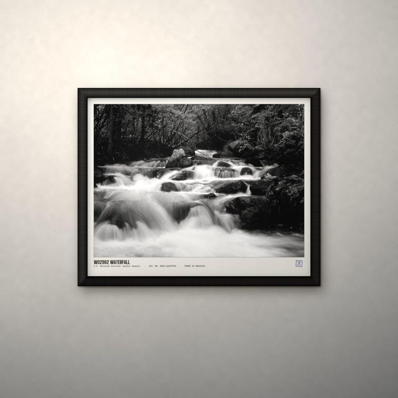 K&ouml;nnte beinhalten: Ein schwarz-wei&szlig; gerahmtes Foto eines Wasserfalls, der &uuml;ber dunkle Felsen in einem Wald flie&szlig;t. Der Druck enth&auml;lt den Text "WD2962 WATERFALL" in der unteren linken Ecke sowie weitere kleine gedruckte Details und ein Logo.