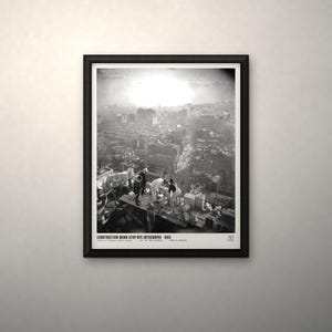 May include: A black and white framed print titled CONSTRUCTION WORK ATOP NYC SKYSCRAPER 1905. The image depicts workers on a high-rise building structure overlooking a city skyline with a bright, hazy sky in the background.