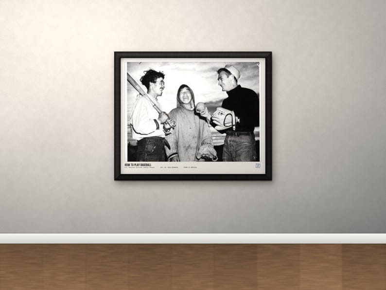May include: A black and white framed photograph depicting three individuals engaged in baseball activities. The left figure holds a bat, the center figure laughs, and the right figure holds a ball and glove. Text at the bottom reads HOW TO PLAY BASEBALL.