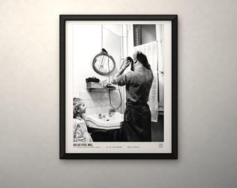 May include: A black and white framed photograph titled SOLLAC STEEL MILL. The image depicts a person using an electric shaver in a bathroom while a child watches. A round mirror, a sink, and a window with a curtain are visible in the background.