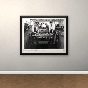May include: A black and white framed photograph depicting two individuals working on airplane engines in a factory setting. The print features the text AIRPLANES - ENGINES - AIRPLANE ENGINES at the bottom, presented in a simple black frame.
