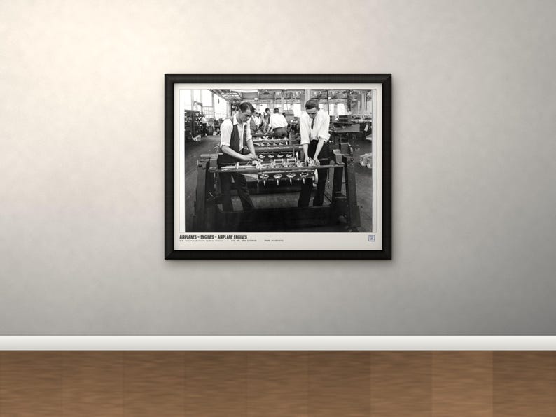 May include: A black and white framed photograph depicting two individuals working on airplane engines in a factory setting. The print features the text AIRPLANES - ENGINES - AIRPLANE ENGINES at the bottom, presented in a simple black frame.