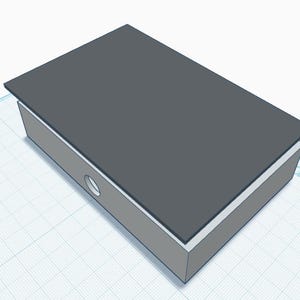 May include: A rectangular box with a dark grey top lid and light grey sides. The front side of the box features a single circular hole centred horizontally. The object is rendered in a three-dimensional digital style with clean, sharp edges.