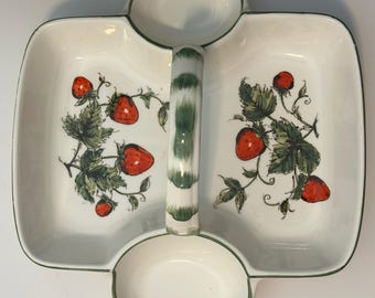 May include: A white ceramic divided serving dish with a central handle featuring green painted accents. The two main rectangular compartments are decorated with illustrations of red strawberries and green leaves, while two smaller circular bowls are plain.
