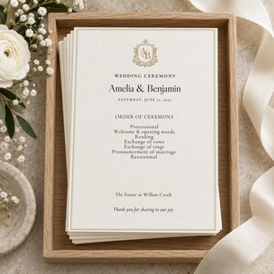 Könnte beinhalten: Ein Stapel cremefarbener Hochzeitszeremonie-Programme mit Goldfolienrändern und einem zentralen Monogramm. Der Text lautet: Wedding Ceremony, Amelia & Benjamin, Saturday, June 12, 2027, Order of Ceremony, The Estate at Willow Creek, Thank you for sharing in our joy.