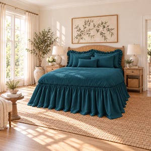 May include: A deep teal bedspread with a ruffled skirt, featuring a matching set of pillows including two large square shams, two rectangular pillows, and one small lumbar pillow, all displayed on a wooden bed frame with a woven headboard.