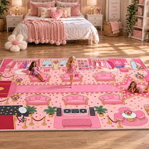 May include: A rectangular area rug featuring a pink-themed fashion studio design with a central runway, multiple pink sofas, vanity stations, and three fashion dolls positioned on the surface. The graphic print includes red carpet areas, star motifs, and various accessories.