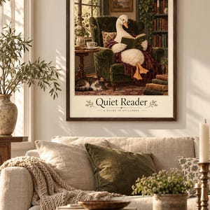 Può includere: Una stampa d'arte incorniciata intitolata Quiet Reader A Study in Stillness che raffigura un'oca bianca con gli occhiali, seduta su una poltrona verde mentre legge un libro, con un gatto che dorme sul pavimento e una libreria.