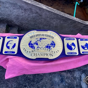 May include: A blue leather World Wrestling Federation Intercontinental Champion belt featuring a large gold center plate with a world map, and smaller gold side plates depicting continents including Antarctica, Europe, Africa, North America, South America, Asia, and Australia.