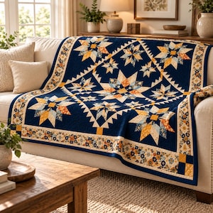May include: A navy blue quilt featuring a repeating star pattern in shades of yellow, orange, and cream. The quilt has a wide border decorated with a small floral print in matching colours and is draped over a light-coloured sofa with two pillows.