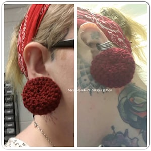 May include: A person with a red bandana and a tattoo on their neck is wearing large, red crocheted ear gauges. The gauges are round and have a textured surface.