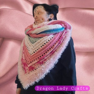 May include: A pink, blue, and white crochet shawl with a fluffy pink fringe. The shawl is draped over a person's shoulders.