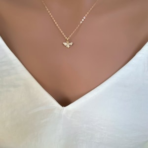 May include: A delicate gold chain necklace with a small bee pendant. The bee is detailed with wings and a body.