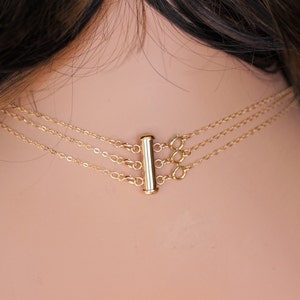 Op de afbeelding: Een gouden ketting met een schuifsluiting. De ketting is gelaagd met drie kettingen van verschillende lengtes.