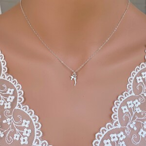 Puede incluir: Un collar de cadena de plata con una pequeña cruz y un dije de cuerno.