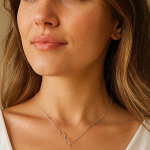 May include: A silver-colored necklace with an infinity symbol and an anchor pendant. The necklace is worn around the neck and hangs down. The anchor pendant is detailed with a small rope and other nautical elements.