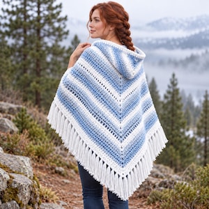 May include: A hooded crochet poncho featuring a V-shaped pattern with alternating horizontal stripes of white and various shades of blue. The garment is finished with long white fringe along the bottom edge, creating a textured appearance.