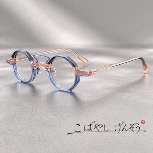 Puede incluir: Gafas hexagonales con una montura degradada que pasa de un azul translúcido en los aros a un color melocotón pálido en las varillas. El puente y las plaquetas están integrados en la estructura. Se observa texto en japonés.