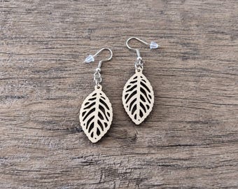 May include: A pair of dangle earrings featuring light-colored wooden leaf-shaped charms with intricate cut-out vein patterns. The charms are attached to silver-toned metal fishhook ear wires with small clear plastic backings for secure placement.