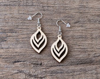 May include: A pair of dangle earrings featuring light-colored, laser-cut wooden pendants in a teardrop shape with internal chevron cutouts. The pendants are attached to silver-toned metal fishhook wires with clear plastic earring backings.